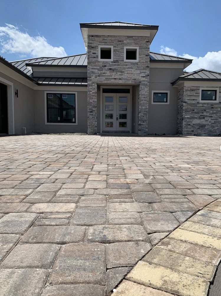 Grand paver driveway leading to a modern stone-front home built by Marblu