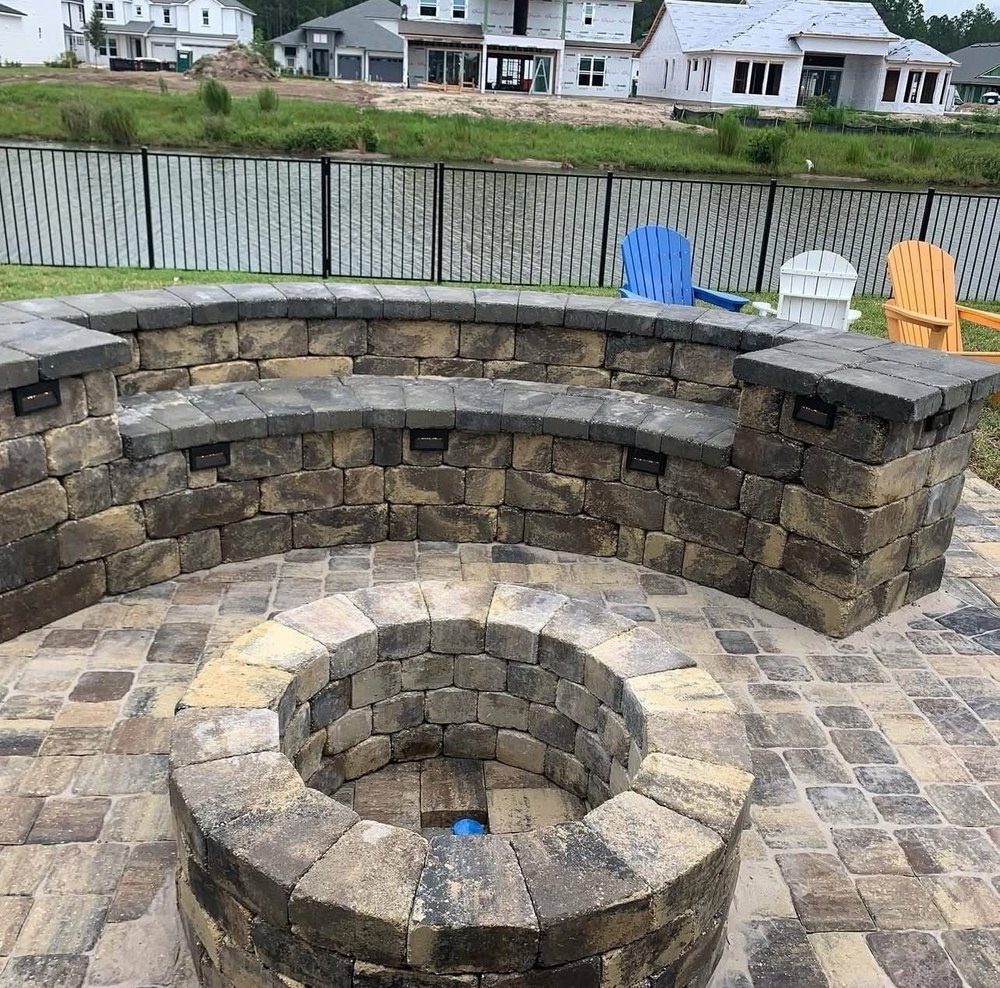 Muro de piedra envolviendo una fogata de mampostería en una terraza de pavers junto al lago