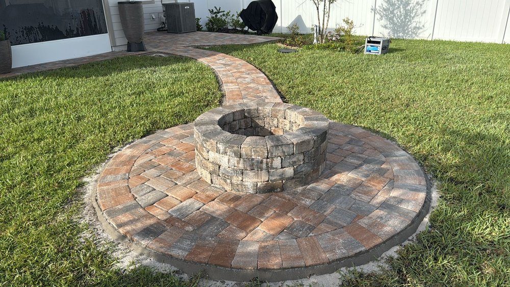 Terraza circular de fogata conectada al césped por un sendero de pavers