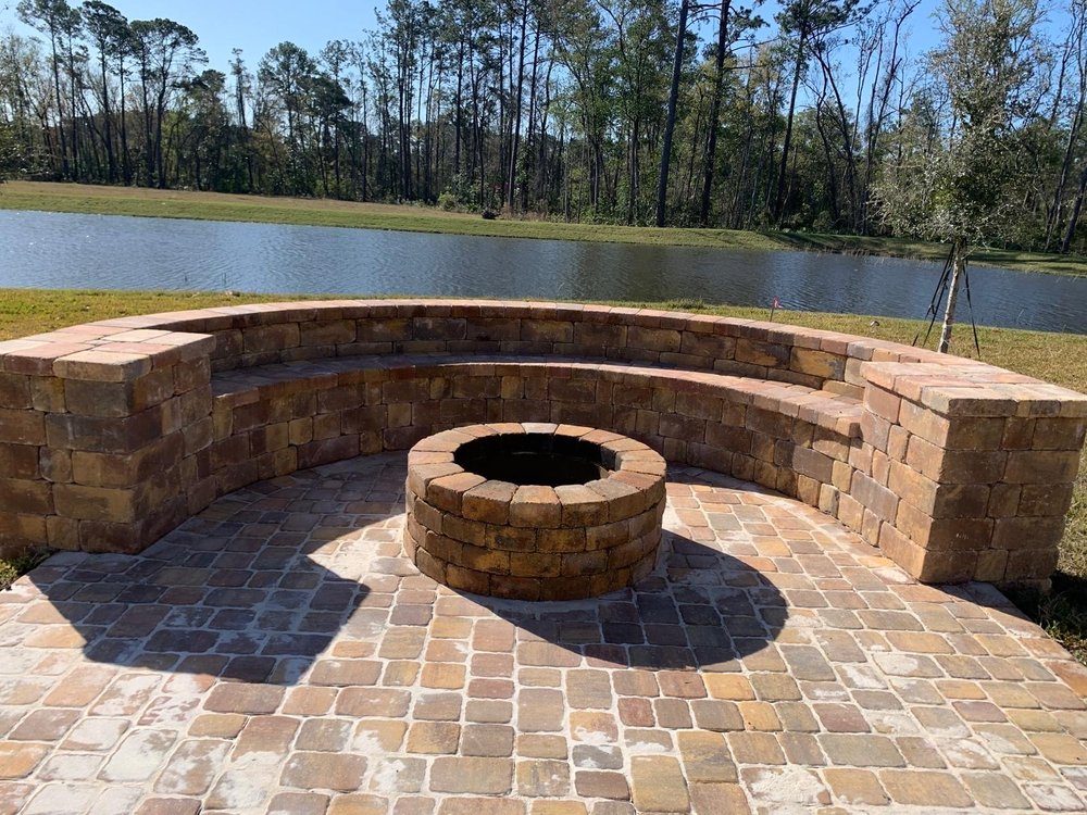 Muro de asientos curvo y fogata redonda en una terraza junto al lago, construidos por Marblu en Jacksonville
