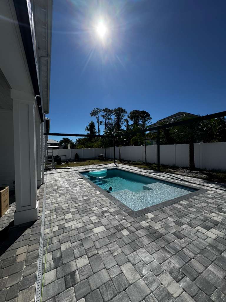 Deck de piscina en pavers grises bajo el intenso sol de Florida con el enclosure en proceso